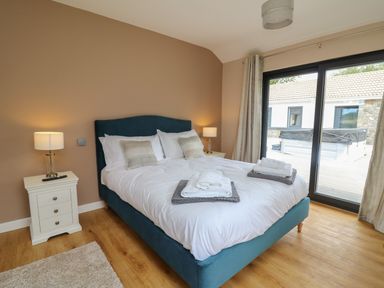 A bedroom with a bed folded towels bedside tables and lamps near sliding glass doors at Heritage in St Clears