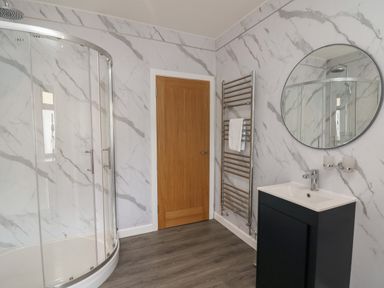 A bathroom with a curved glass shower enclosure a wooden door a towel rack a sink with a cabinet and a round mirror at Heritage in St Clears