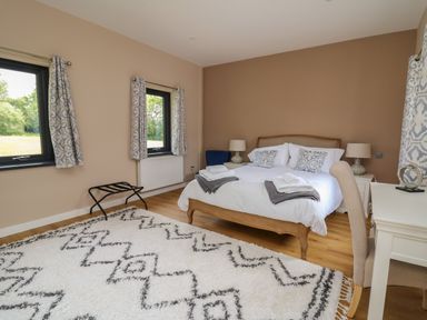 A bedroom with a double bed two windows with patterned curtains a white desk and chair and a patterned rug on the floor at Heritage in St Clears