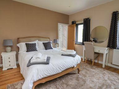 A bedroom with a double bed bedside tables lamps a dressing table with a chair and an en suite shower at Heritage in St Clears