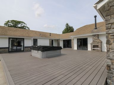 An outdoor patio area with a covered hot tub stone fireplace and sliding glass doors at Heritage in St Clears