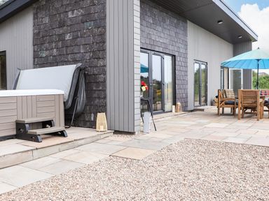 An outdoor patio area with a hot tub and wooden dining table with chairs under a blue umbrella at Pine Marten in Dornoch