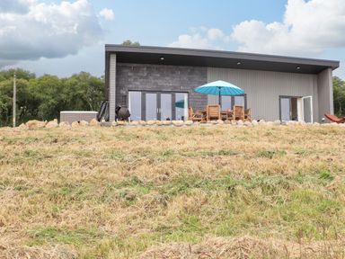A modern house with outdoor furniture and an umbrella on a patio surrounded by a stone border at Pine Marten in Dornoch