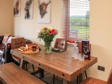 A dining table with bread flowers and whisky in a room with animal paintings and a window with wooden blinds at Pine Marten in Dornoch