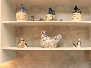 A kitchen shelf with bottles labeled vodka gin and port and ceramic bird decorations including a large hen and four puffins at Pine Marten in Dornoch