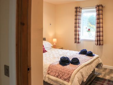 A bedroom with a bed with rolled towels and a window with curtains at Pine Marten in Dornoch