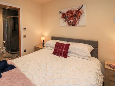 A bedroom with a bed white bedding bedside tables lamps and a bathroom visible through an open door at Pine Marten in Dornoch