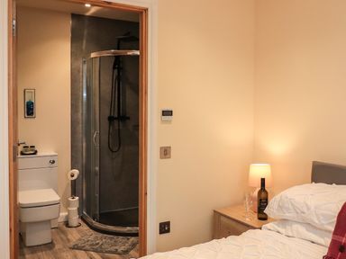 A bedroom with a bedside table lamp and bottle next to a bed with an en suite bathroom featuring a shower and toilet at Pine Marten in Dornoch