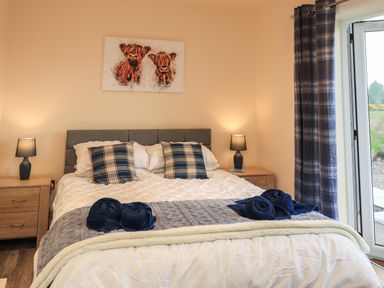 A bedroom with a bed with plaid pillows bedside tables with lamps and a door with plaid curtains at Pine Marten in Dornoch