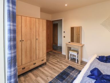 A bedroom with a wooden wardrobe a dressing table with a mirror and a stool a bed with blue towels and a blue plaid curtain at Pine Marten in Dornoch