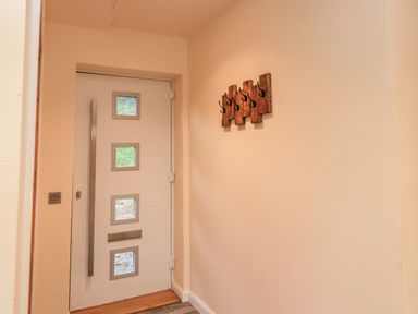 A white front door with four square windows and a metal handle next to a wall with wooden coat hooks at Pine Marten in Dornoch