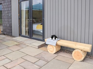 An outdoor patio with a wooden bench holding a stuffed animal and a blanket next to glass double doors at Pine Marten in Dornoch