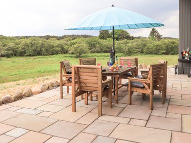 An outdoor patio with a wooden table and chairs under a blue umbrella overlooking a green field at Pine Marten in Dornoch