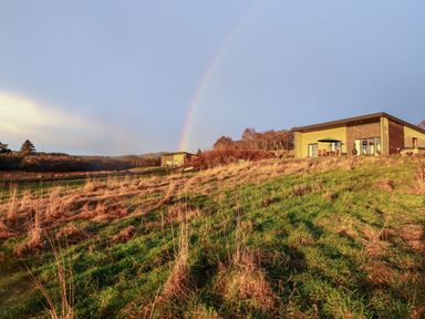 A grassy hillside with two houses and a rainbow in the sky at Pine Marten in Dornoch
