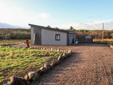 A modern single-story house with a gravel driveway and stone border at Pine Marten in Dornoch