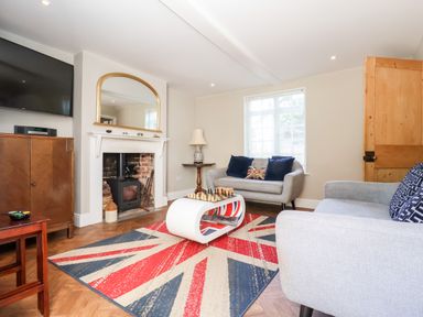 A living room with a fireplace a wall-mounted TV two sofas and a rug with a Union Jack design at Cavan Cottage in Yoxford