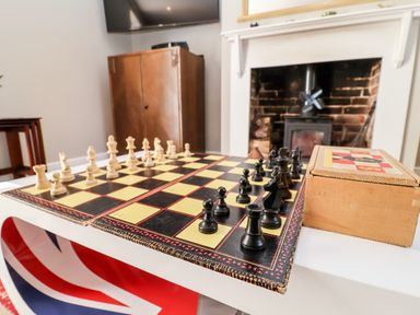 A chessboard with chess pieces set up on a table in a room with a fireplace and wooden furniture at Cavan Cottage in Yoxford