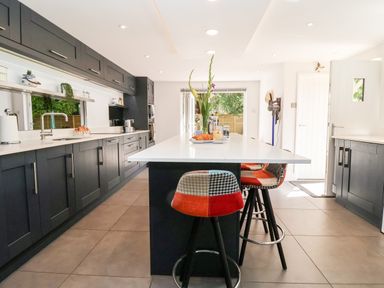 A kitchen with dark cabinets a white island with stools and a sliding door at Cavan Cottage in Yoxford