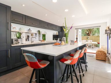A kitchen with a large island and four stools and an open door leading to an outdoor dining area at Cavan Cottage in Yoxford