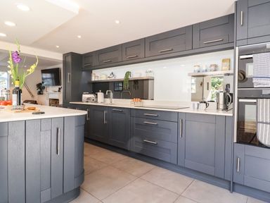 A kitchen with gray cabinets a white countertop a vase with flowers and various kitchen appliances at Cavan Cottage in Yoxford