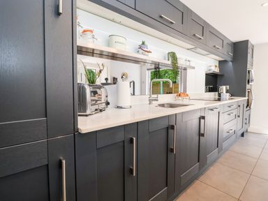 A kitchen with dark cabinets white countertops a stainless steel toaster a paper towel holder a sink and eggs on a tray at Cavan Cottage in Yoxford