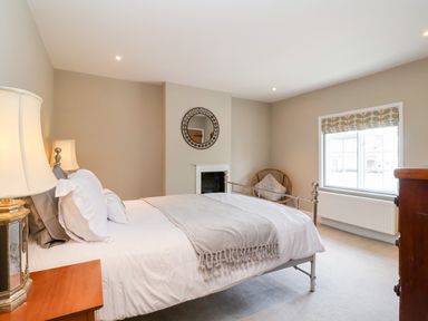 A bedroom with a bed lamp a chair a window and a dresser at Cavan Cottage in Yoxford