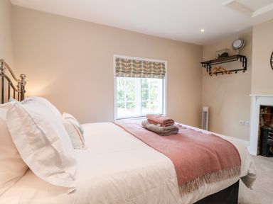 A bedroom with a bed covered with white linens and pink throw near a window with patterned blind at Cavan Cottage in Yoxford