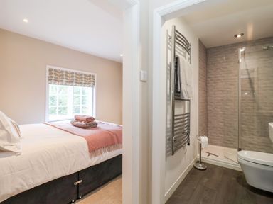 A bedroom with a bed and window next to a bathroom with a shower and towel rack at Cavan Cottage in Yoxford