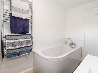 A bathroom with a bathtub a towel rack with towels and a door at Cavan Cottage in Yoxford