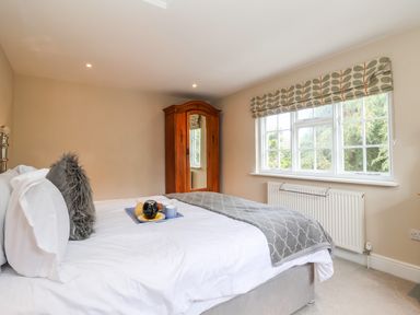 A bedroom with a bed featuring pillows and a blanket a wooden wardrobe and a window with patterned blinds at Cavan Cottage in Yoxford