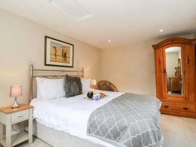 A bedroom with a bed lamp a chair an armoire and a framed picture at Cavan Cottage in Yoxford