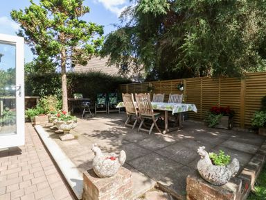 An outdoor patio with a dining table and wooden chairs surrounded by potted plants and a wooden fence at Cavan Cottage in Yoxford
