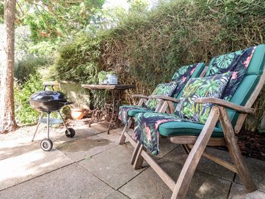An outdoor patio with wooden chairs with cushions and a small round barbecue grill near a table with a plant at Cavan Cottage in Yoxford