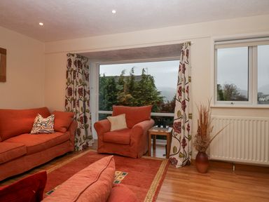 A sitting room with orange sofas and armchair a wooden side table and patterned curtains at Fairfield View in Ambleside