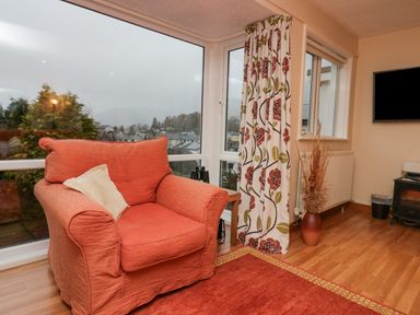 A living room with an orange armchair a floral curtain a wooden floor and a television at Fairfield View in Ambleside