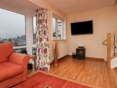 A corner of a living room with an orange armchair a floral curtain a wall-mounted television and a small stove at Fairfield View in Ambleside
