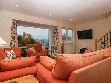 A living room with orange sofas a wall-mounted television and patterned curtains at Fairfield View in Ambleside