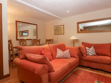 A living room with two orange sofas pillows a lamp and a dining table with chairs and mirrors on the wall at Fairfield View in Ambleside
