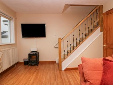 A living room with a wall-mounted television a small heater a staircase with wooden railing and part of a red sofa at Fairfield View in Ambleside
