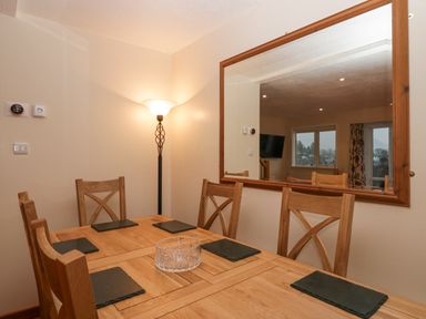 A dining area with a wooden table, six chairs, black placemats, a glass bowl, a floor lamp, and a large wall mirror at Fairfield View in Ambleside