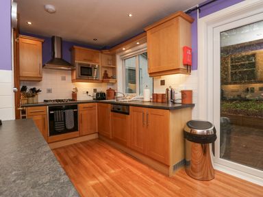 A kitchen with wooden cabinets a gas stove a microwave a sink and a stainless steel trash can at Fairfield View in Ambleside