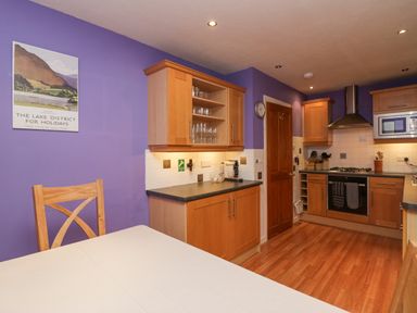 A kitchen with wooden cabinets a gas stove a microwave a wooden door and a table with a chair at Fairfield View in Ambleside