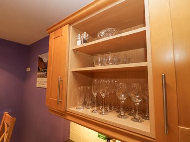 A wooden kitchen cabinet with shelves holding glassware and salt and pepper shakers at Fairfield View in Ambleside