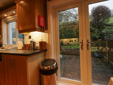 A kitchen corner with wooden cabinets a countertop a kettle canisters a paper towel holder a trash bin and glass doors leading to a garden at Fairfield View in Ambleside