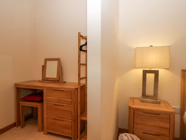 A wooden dressing table with mirror and stool and a wooden nightstand with lamp in a bedroom at Fairfield View in Ambleside