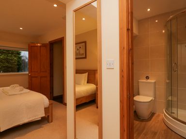 A bedroom with a bed and towels next to an open door leading to a bathroom with a toilet and shower at Fairfield View in Ambleside