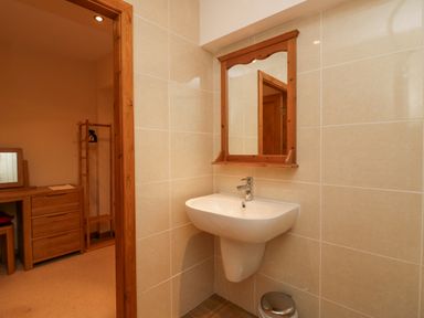 A bathroom with a wall-mounted sink and mirror next to a doorway leading to a bedroom with wooden furniture at Fairfield View in Ambleside
