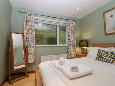A bedroom with a bed set with towels beside a window with floral curtains and a standing mirror at Fairfield View in Ambleside