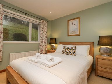 A bedroom with a double bed two bedside tables lamps and a window with floral curtains at Fairfield View in Ambleside