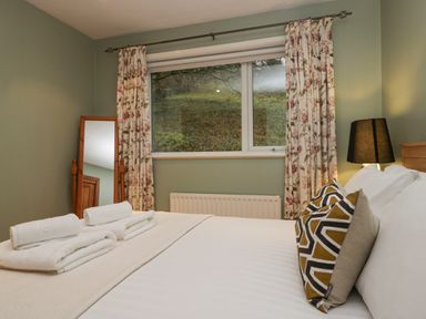 A bedroom with a bed with pillows and folded towels by a window with floral curtains at Fairfield View in Ambleside